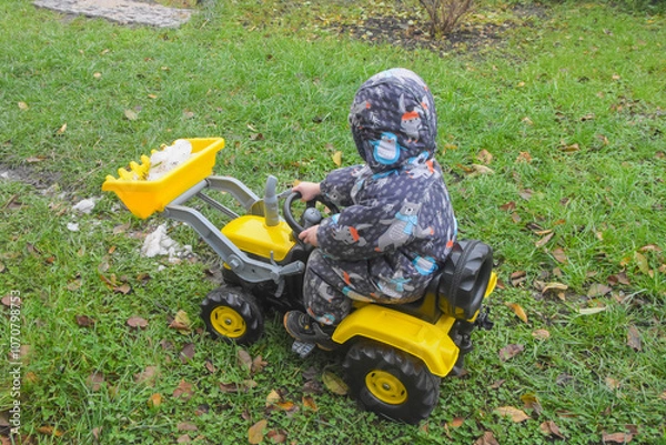 Fototapeta a child boy on a wheeled bulldozer tractor removes snow with a snow plow, photo without filters