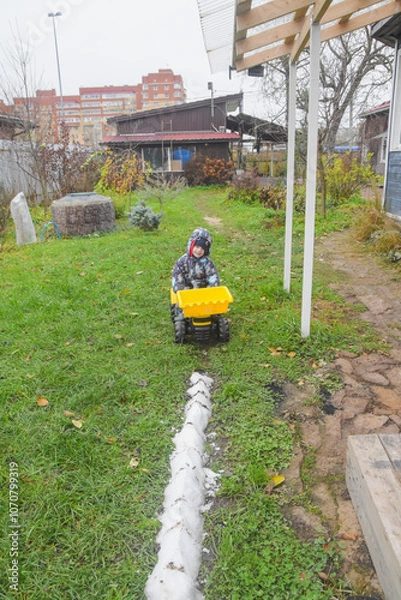 Fototapeta a child boy on a wheeled bulldozer tractor removes snow with a snow plow, photo without filters