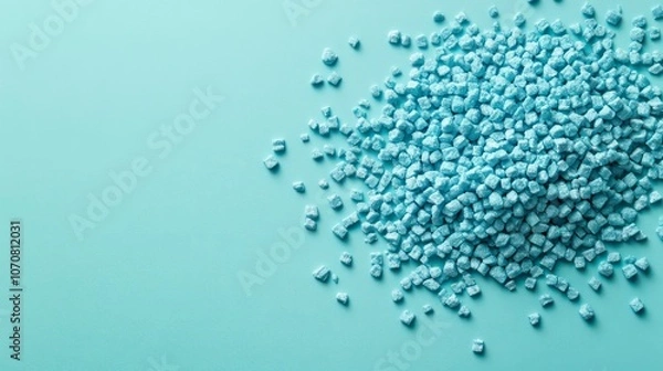 Fototapeta A pile of small blue plastic pellets on a light background, likely for manufacturing use.
