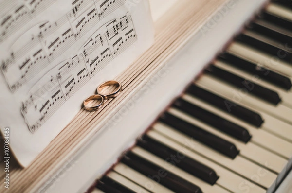 Obraz Pair golden rings on classic, piano keyboard with music notes. Wedding accessories. Black and white background, selective focus 