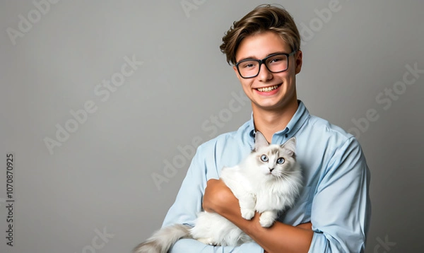 Fototapeta A smiling young man holding a fluffy white Ragdoll cat, capturing a heartwarming moment of companionship and affection between the two, with the cat’s striking blue eyes and soft fur adding to the cha