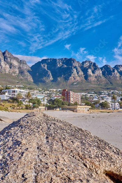 Obraz Landscape, rock and beach with buildings, city and sky with mountain view, outdoor and summer in nature. Stone, boulder and environment with sand, hill and urban expansion on horizon in South Africa