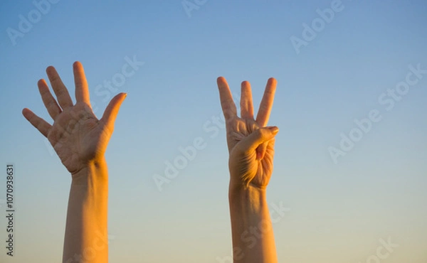 Fototapeta Woman hands showing or doing number eight gesture on blue summer sky background. Counting down, eight fingers up concept idea.	