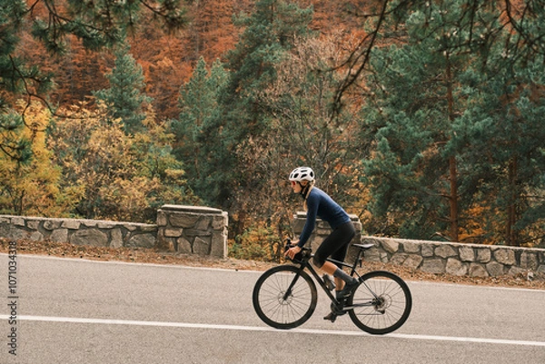 Obraz Woman cyclist rides road bike through scenic autumn landscape. Vibrant fall foliage provides stunning backdrop. Active lifestyle and outdoor adventure. Romania. Carpathian Mountains. Transylvania