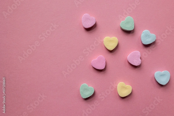 Fototapeta flat lay of scattered pastel colored candy hearts in pink, green, and yellow against a pink background with copy space available; valentines day themed