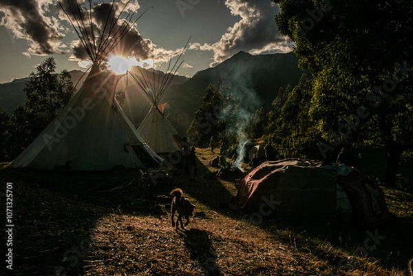 Fototapeta Native community with people in a landscape with teepee and temazcal in a sunrise with the sun rising over the mountains. 