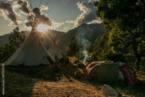 Fototapeta Native community with people in a landscape with teepee and temazcal in a sunrise with the sun rising over the mountains. 