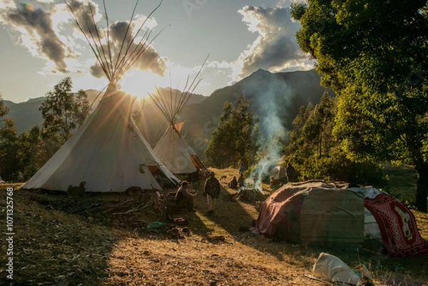 Fototapeta Native community with people in a landscape with teepee and temazcal in a sunrise with the sun rising over the mountains. 