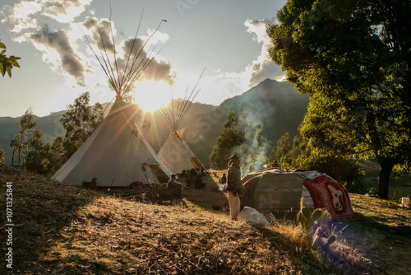 Fototapeta Native community with people in a landscape with teepee and temazcal in a sunrise with the sun rising over the mountains. 