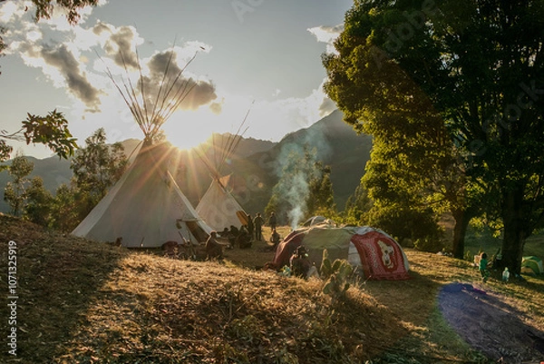 Fototapeta Native community with people in a landscape with teepee and temazcal in a sunrise with the sun rising over the mountains. 