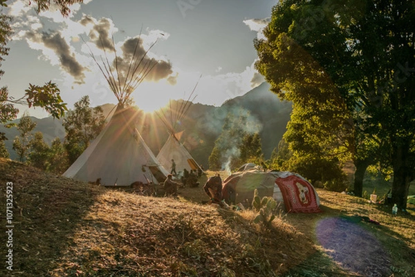Fototapeta Native community with people in a landscape with teepee and temazcal in a sunrise with the sun rising over the mountains. 
