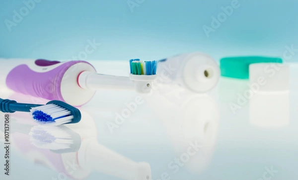 Obraz Electric and classic toothbrushes on reflective surface and light blue background.