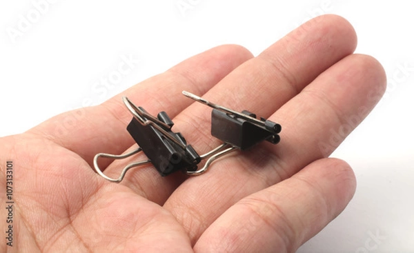 Fototapeta Pair of Small Binder Clip on Hand. Two small black binder clips placed next to each other on hand in white background