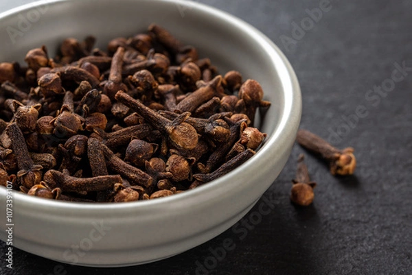 Fototapeta Whole cloves spice in a bowl over black background. Dry clove buds in a gray ceramic bowl macro. Cooking, herbal medicine and spice concept.
