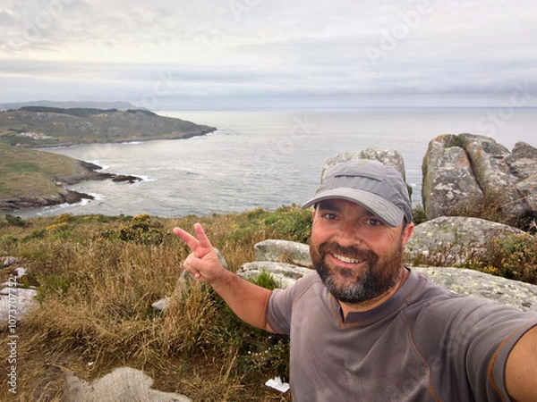 Obraz A man in cap taking a selfie on a hill with the sea in the background