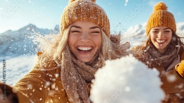 Fototapeta Two joyful friends in warm clothing throw snowballs playfully in a winter wonderland, surrounded by snow-covered mountains, exuding pure joy and happiness.