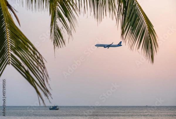 Obraz Tropical scene with an airplane flying over the sea at sunset, with palm leaves and a boat in the foreground