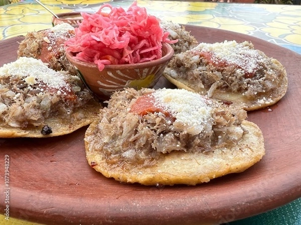 Fototapeta Traditional garnachas served on a clay plate at a restaurant in Oaxaca, Mexico. Deep-fried beef on masa with salsa and cheese. Close up from the side.