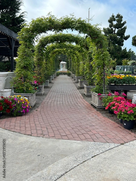 Obraz A picturesque brick-paved pathway bordered by lush flower beds in full bloom, with vibrant, colorful flowers flanking both sides.