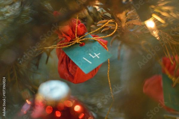 Fototapeta Little red present hanging in the Christmas tree with the number 14 on it.