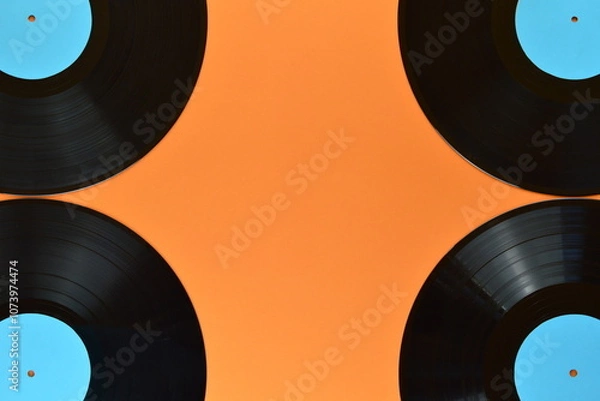 Fototapeta four old black vinyl records with blank cyan labels on the edges of orange background and copy space in the middle