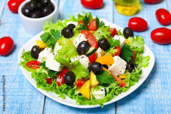 Fototapeta Greek salad with fresh vegetables, feta cheese and black olives on a wooden background