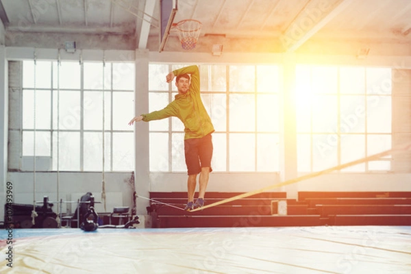 Fototapeta Man slacklining walking and balancing on a rope, slackline in a sports hall