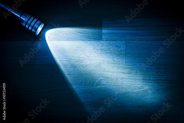 Obraz Flashlight and a beam of light in darkness. A modern led light with bright projection on dark wood table. Surface with copy space.