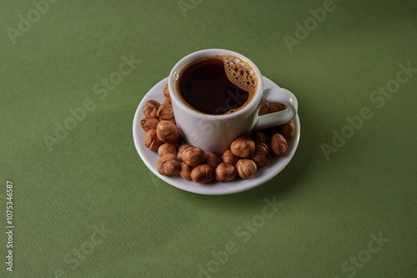 Fototapeta Enjoying a warm cup of coffee accompanied by roasted hazelnuts on a green tabletop in a cozy setting