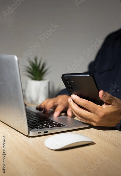Fototapeta Programmer holding smartphone and typing on laptop keyboard: cybersecurity and privacy concept