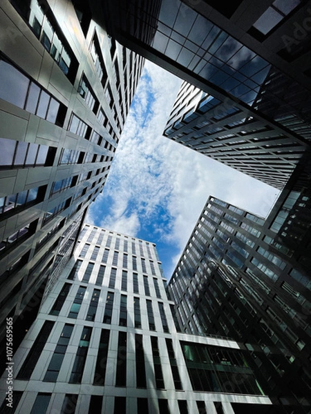 Fototapeta View of office skyscrapers with reflections against a cloudy sky, shot from below.