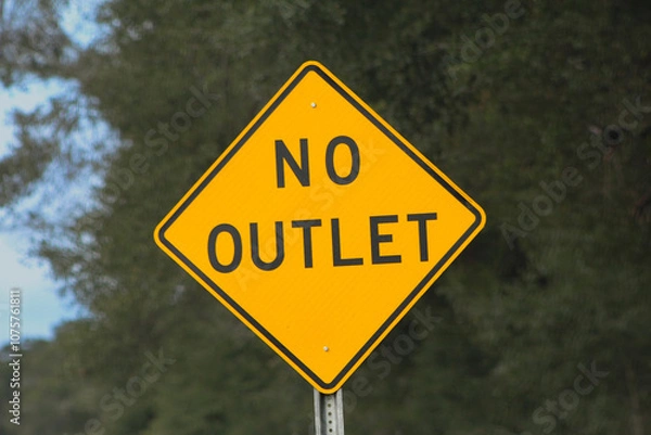 Obraz A bright yellow "No Outlet" road sign stands prominently against a blurred natural background. Sign warns drivers of a dead-end or limited exit route ahead, symbolizing caution or restriction.