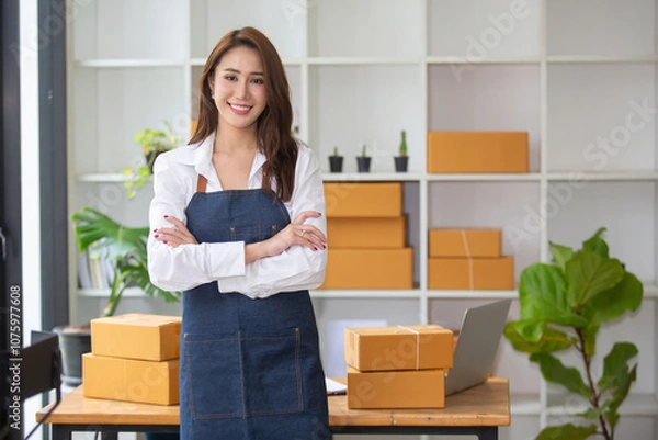 Fototapeta Beautiful business woman Happy working online shopping at her store. Through phone, computer, young woman seller prepares parcel boxes to send to customers. online sales ecommerce