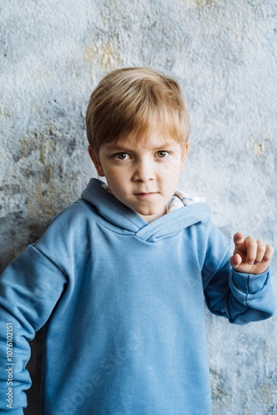 Obraz A young boy donned in a bright blue hoodie is standing in front of a wall, possibly admiring his surroundings or simply enjoying the moment and feeling a sense of happiness and joy