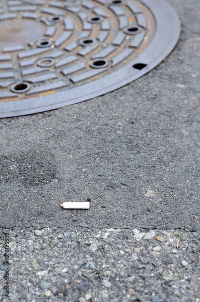 Fototapeta 道路上にポイ捨てされたタバコとすぐ近くにあるマンホールのある風景
