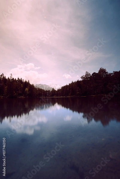 Fototapeta Calm lake reflecting mountains and sky during golden hour in a serene landscape