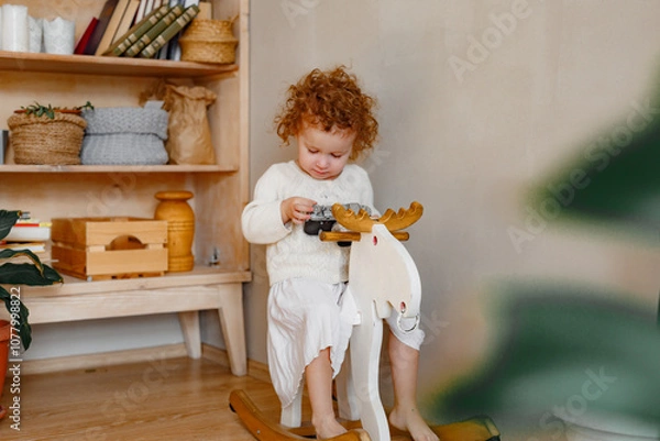Obraz Portrait of funny young retro girl photographer in white clothes at home background, holds camera in hands, looks into camera serious