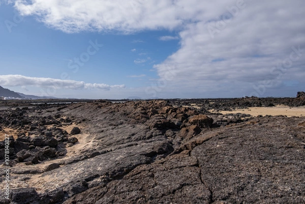 Obraz White sand beach with solidified volcanic lava flows, black rocks. Mountains in the background and sky with big white clouds. Caletón Blanco, Lanzarote, Canary Islands, Spain