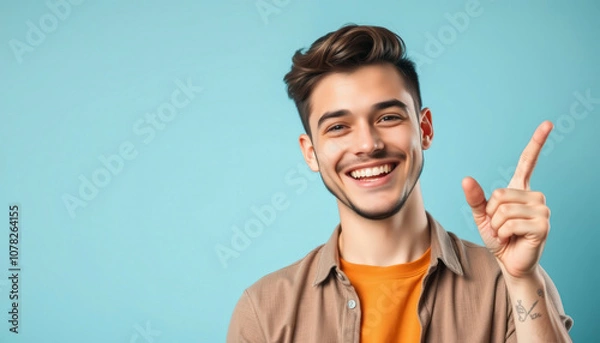 Fototapeta Happy young man pointing finger up with a joyful expression on a light blue