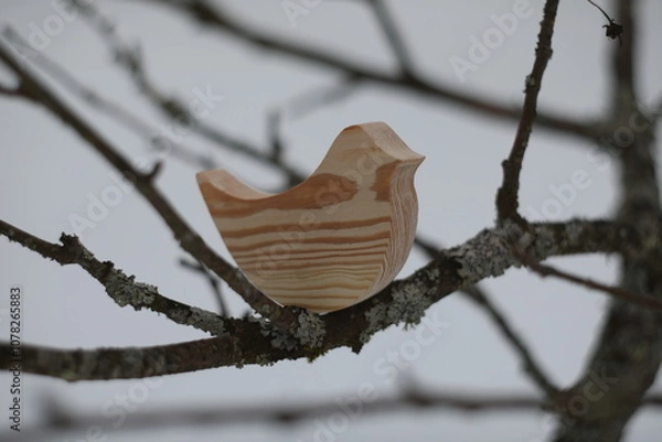 Fototapeta Wooden handmade toy bird on the tree branch on a winter day. Hello Spring concept. Winter landscape. Helping animals feed.
