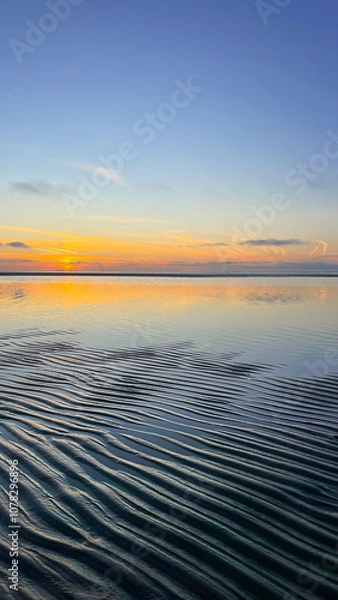 Fototapeta Natural background. Sunset on the shore of the mole. Low tide. A marine pattern on the sand. Calm. The landscape. Landscape. The sky is reflected in the water.
