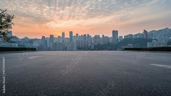 Obraz An empty asphalt road with a city skyline and sunrise in the background.