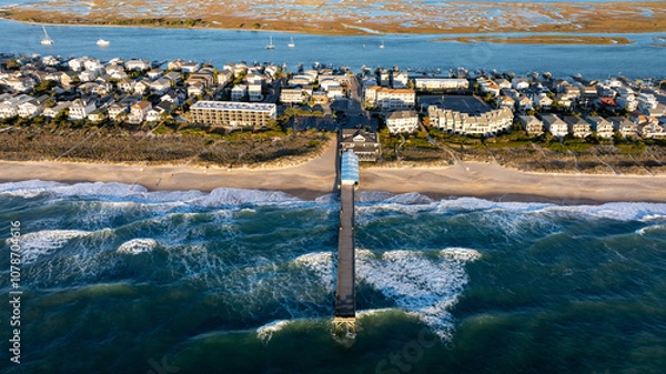 Obraz Aerial view of a pier stretching into the ocean at Wrightsville Beach, NC, surrounded by beachfront residential buildings and an inlet in the background.