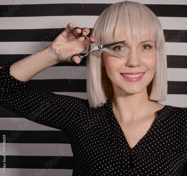 Fototapeta Smiling beautiful woman holding a pair of scissors in his hand. The concept of beauty and fashion