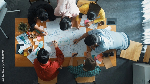 Fototapeta Group of business people writing and making mind map to brainstorming marketing idea at meeting. Top aerial view of investors sharing plan or strategy by using sticky notes. Top view. Convocation.