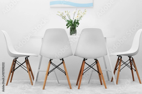 Fototapeta Modern dining room. White chairs and table with bouquet of flowers, abstract picture on the wall