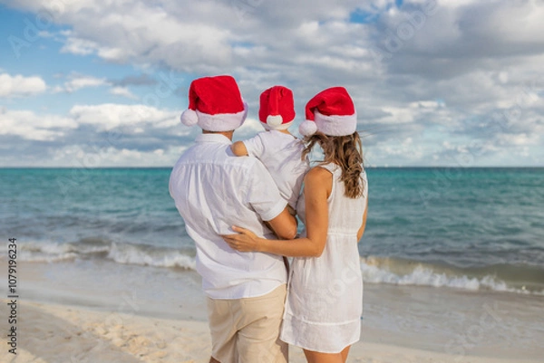 Fototapeta Happy family celebrates Christmas on the beach. Mom, dad and son in holiday hats on the beach celebrate the New Year