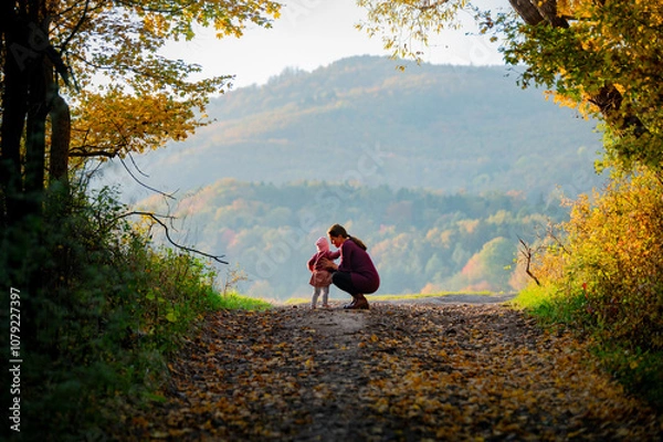 Fototapeta Mother and Daughter Walk Hand-in-Hand Through an Enchanting Autumn Landscape, Creating Memories