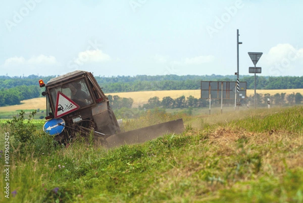 Fototapeta Tractor with a mechanical mower mowing grass on the side of the asphalt road