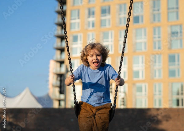 Fototapeta Kid swinging on chain swing on city kids playground. Swing ride. Cute child having fun on a swing on summer sky background. Blonde little boy swings at kid playground. Child swinging high.